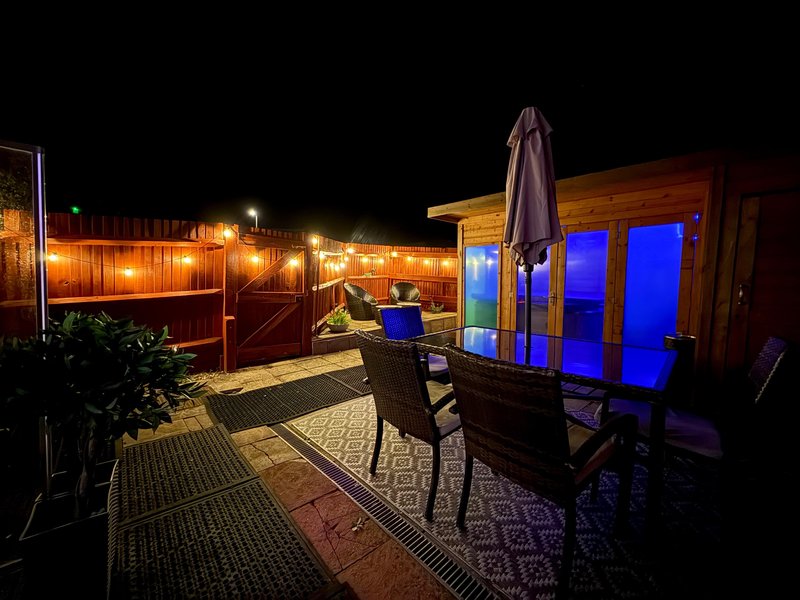 Outdoor patio at night with string lights, umbrella, seating area and garden furniture