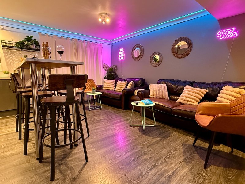 Modern lounge with leather sofas, bar seating, piano, and colorful ambient lighting