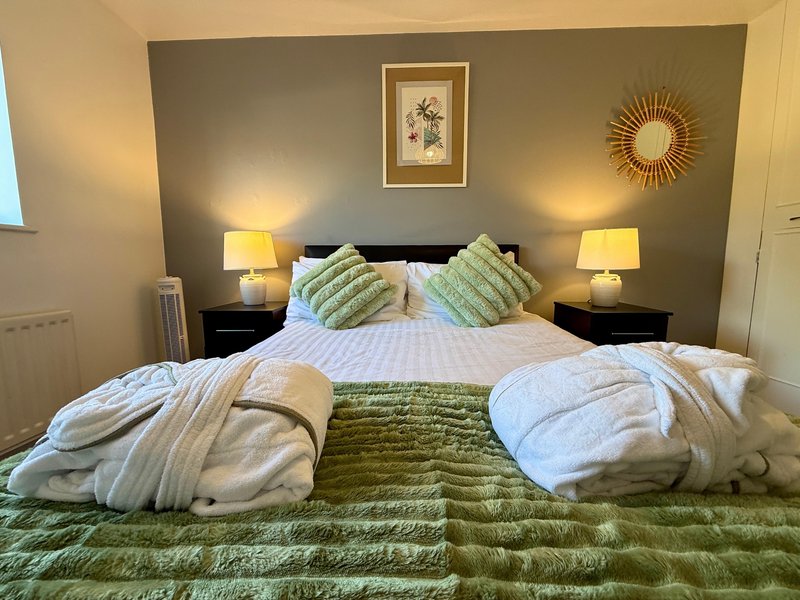 Bedroom with double bed, green bedding, two bedside lamps, framed wall art and sunburst mirror