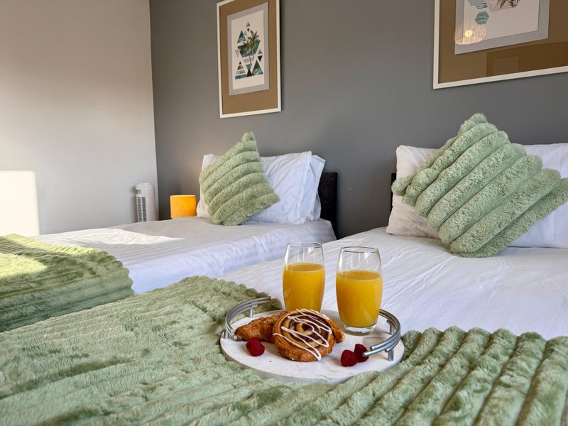 Bedroom with two beds, green quilted cushions, framed wall art, and breakfast tray with juice and pastries