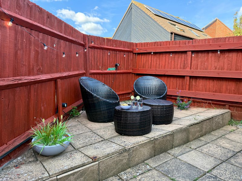 Enclosed patio area with red wooden fence, black wicker seating, and potted plants