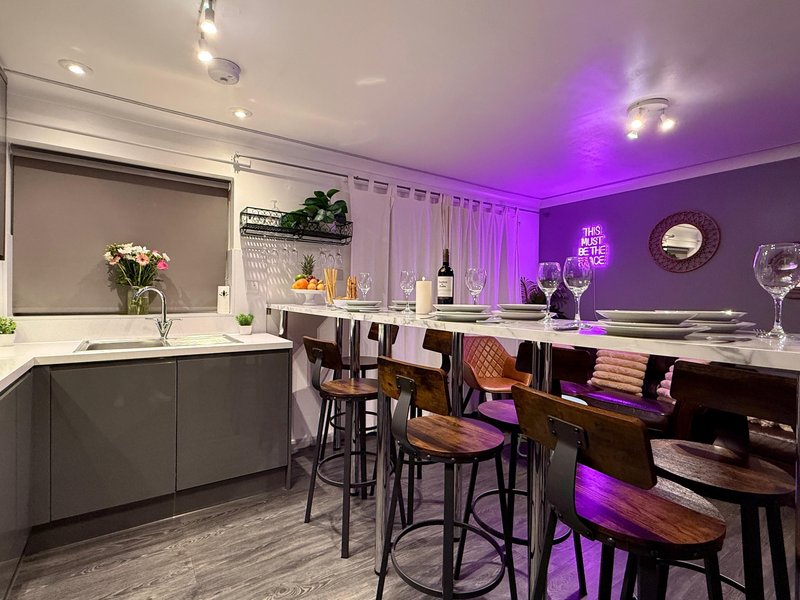 Modern kitchen and bar area with purple ambient lighting, white countertops, and bar seating