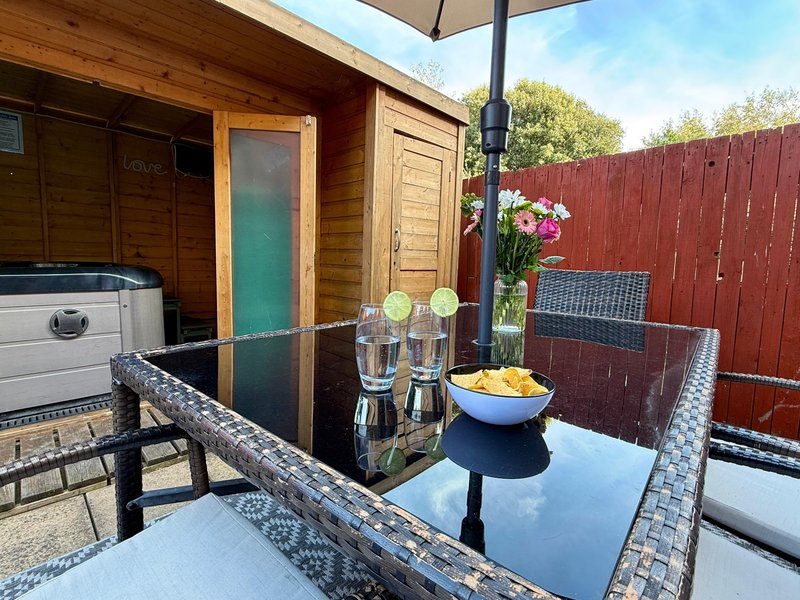 Outdoor patio area with dining table, flowers, glasses, and hot tub beside wooden cabin