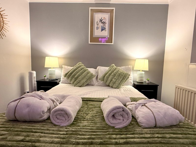 Modern bedroom with double bed, purple pillows, green bedding, bedside lamps and framed wall art