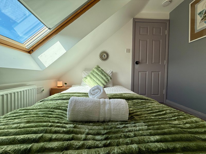Attic bedroom with skylight, green striped bedding, rolled towel, and gray door