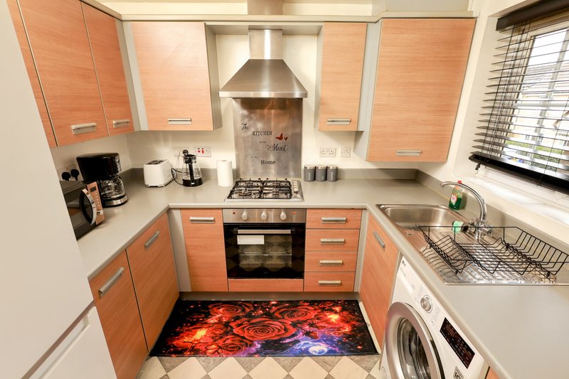 Modern kitchen with orange cabinets, gas hob, oven, and washing machine
