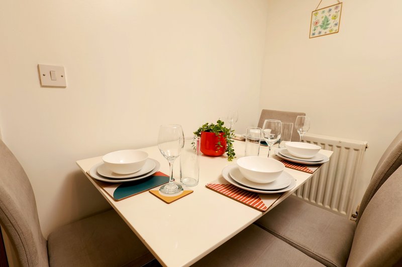 Dining table set for two with place settings, glasses, and red flower centerpiece