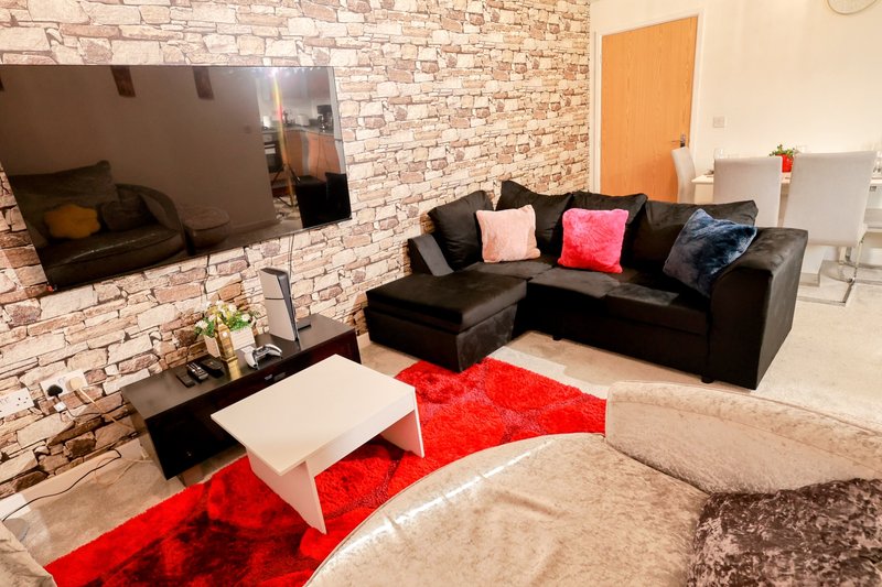 Modern living room with black leather sofa, red area rug, TV on brick wall, and white coffee table