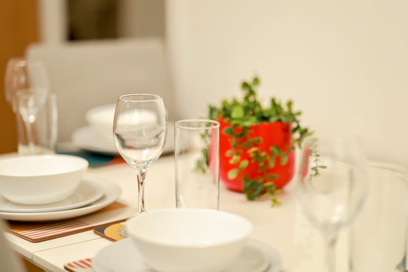 Formal dining table set with white plates, glassware, and red potted plant centerpiece