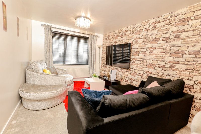 Living room with black leather sofa, cream armchair, brick accent wall and wall-mounted TV