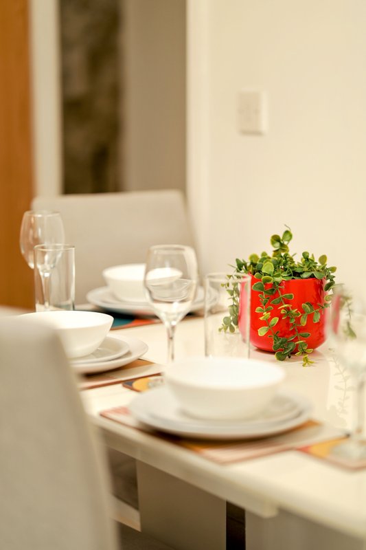 Dining table set with white plates, glasses, and red potted plant decoration