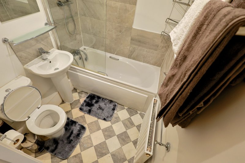 Modern bathroom with toilet, sink, shower enclosure, and checkered floor mat