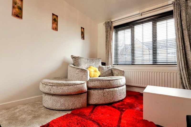 Modern sitting area with two curved upholstered armchairs, red rug, and large window with blinds and curtains