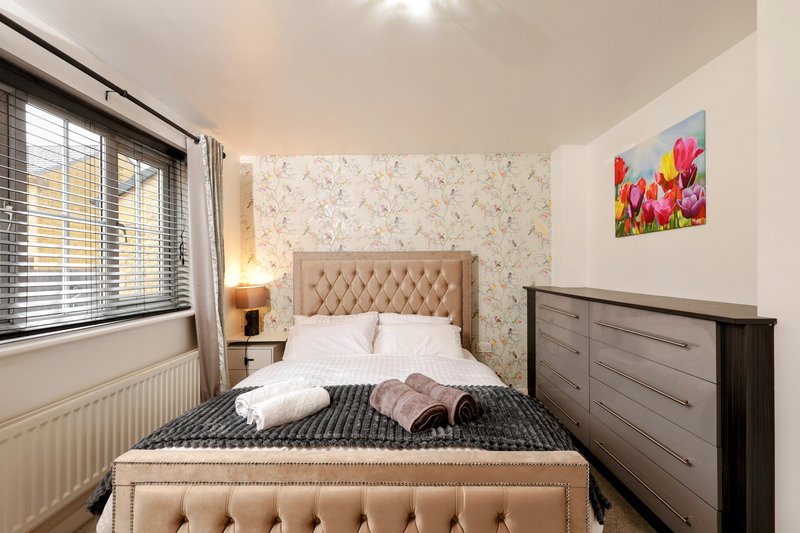 Bedroom with double bed, beige headboard, dark wood dresser, floral wallpaper and window