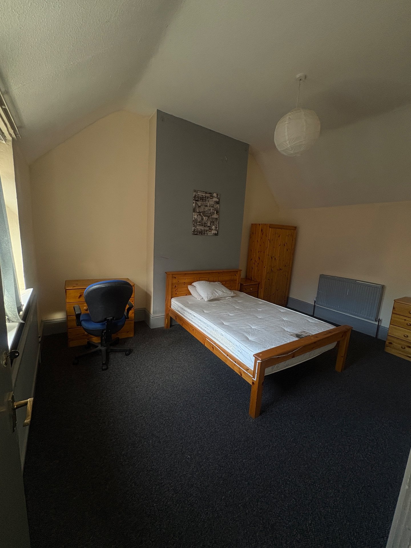 Bedroom with wooden bed frame, blue chair, dark carpet and angled ceiling