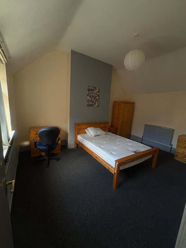 Bedroom with wooden bed frame, blue chair, dark carpet and angled ceiling
