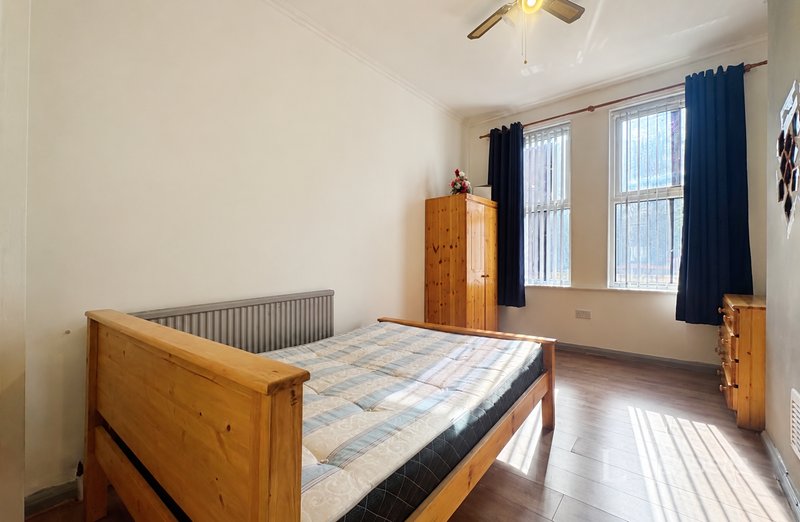 Bright bedroom with wooden bed frame, blue curtains, radiator and wooden wardrobe