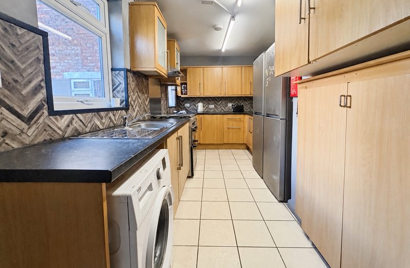 Galley kitchen with wooden cabinets, black countertops, stainless steel appliances and tile flooring