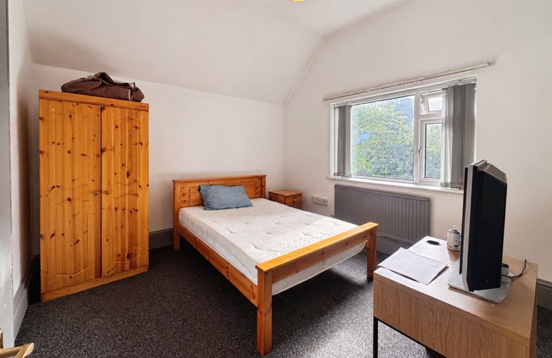 Bedroom with wooden bed frame, pine wardrobe, window, radiator and desk area
