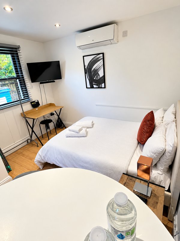 Bright bedroom with double bed, desk, TV, air conditioning unit and wooden flooring