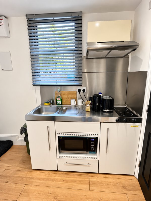 Compact white kitchen with stainless steel countertop, microwave, sink and window blinds