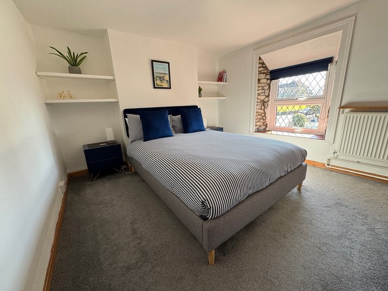 Bright bedroom with double bed, blue cushions, floating shelves, window and radiator