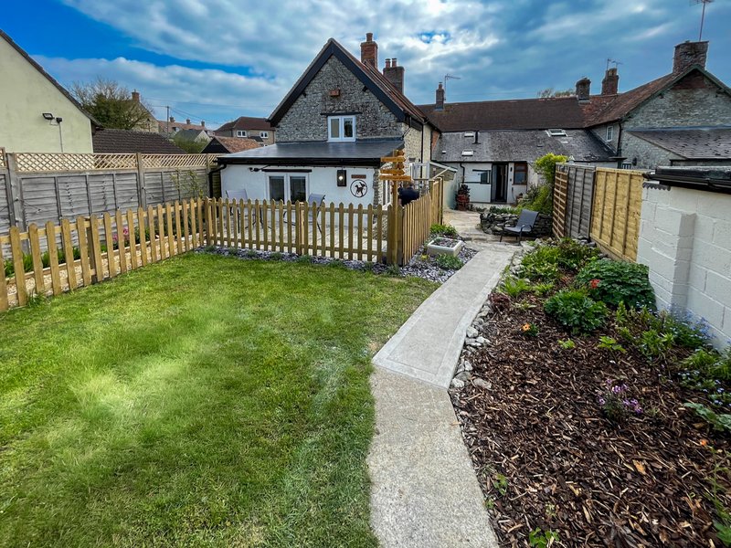 Rear garden with lawn, wooden fence, patio area and stone cottage backdrop