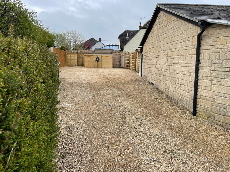 Gravel driveway with wooden fencing, stone-built property and manicured hedge