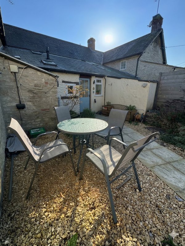 Outdoor patio area with round table, chairs, stone cottage and garden