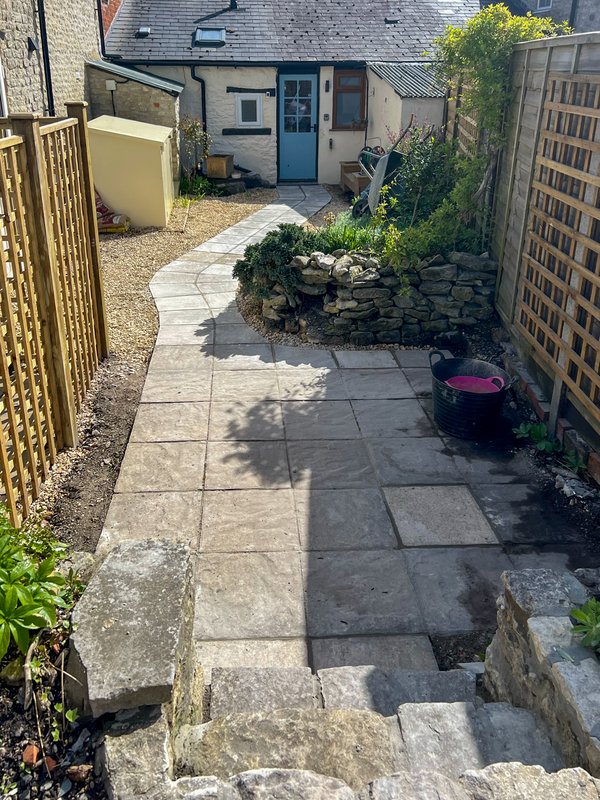 Rear garden patio with stone paving, wooden fences, planted beds and outdoor seating area