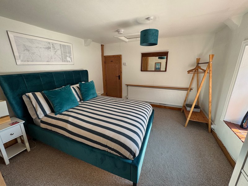 Bedroom with teal upholstered bed, striped bedding, wooden clothing rack, and framed wall art