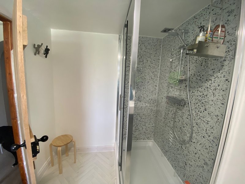 Modern bathroom with walk-in shower, terrazzo tiles, wooden stool, and white walls