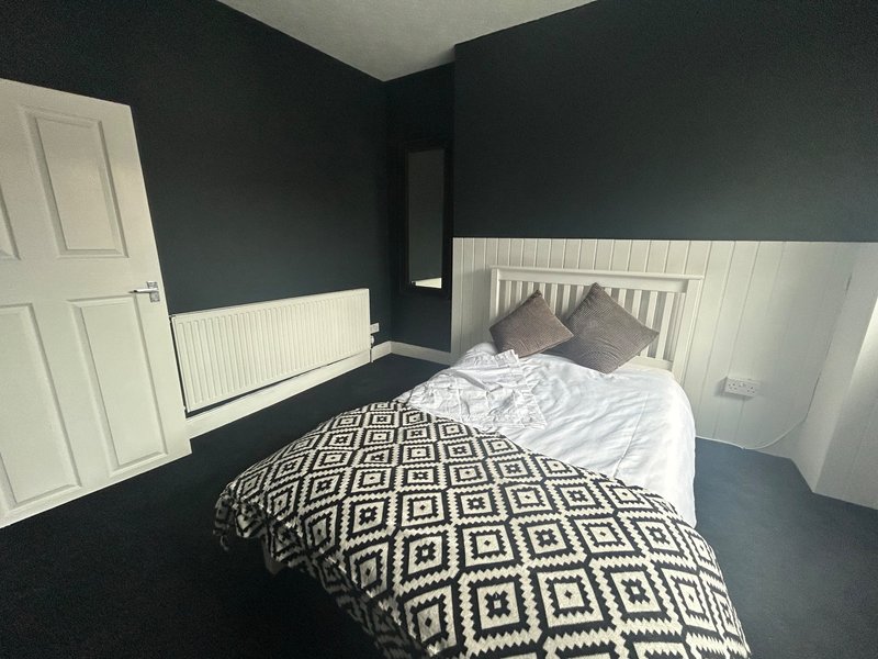 Modern bedroom with double bed, geometric bedding, dark walls and white panelling,