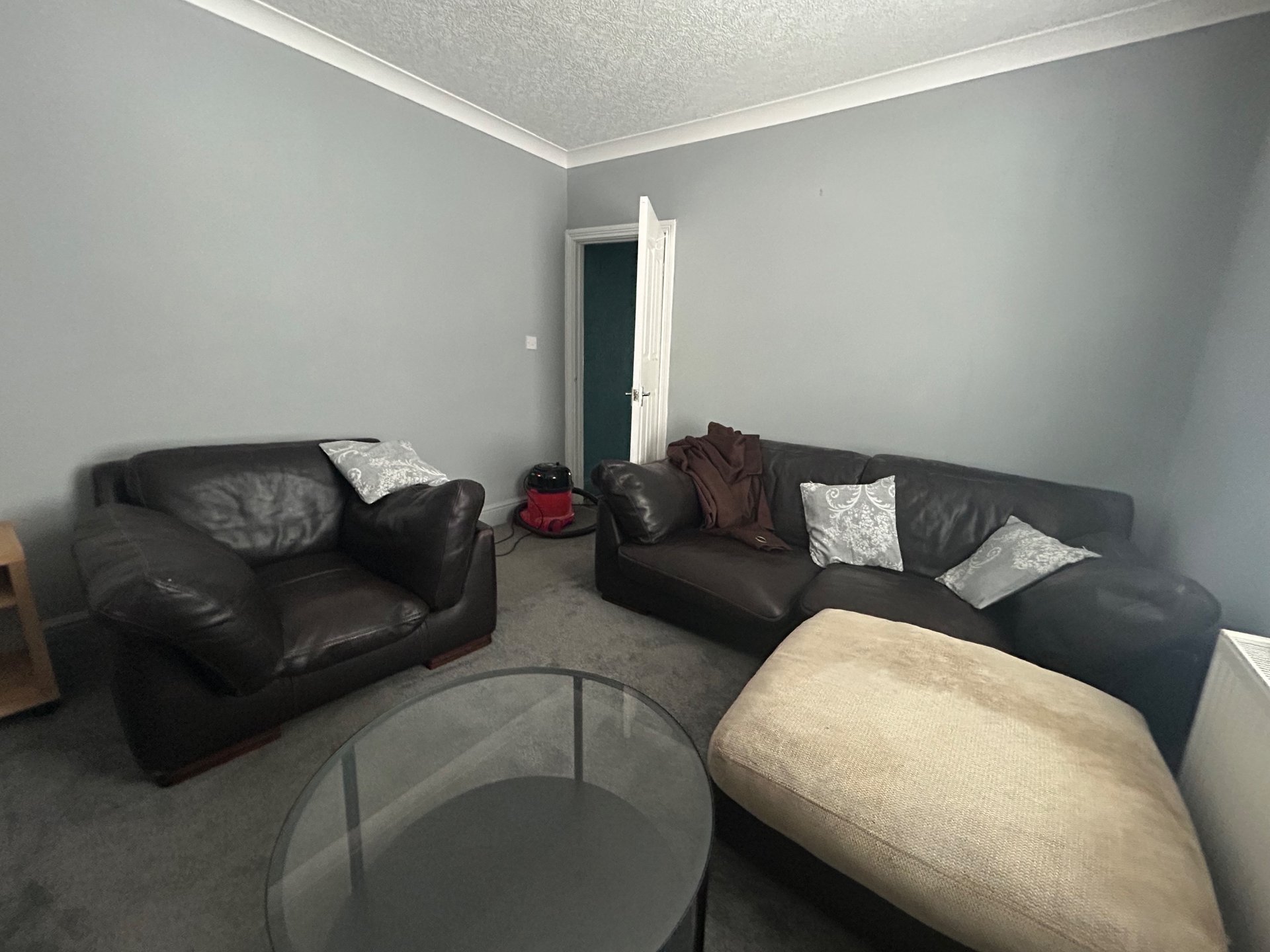 Living room with two black leather sofas, glass coffee table, beige ottoman and grey carpeting