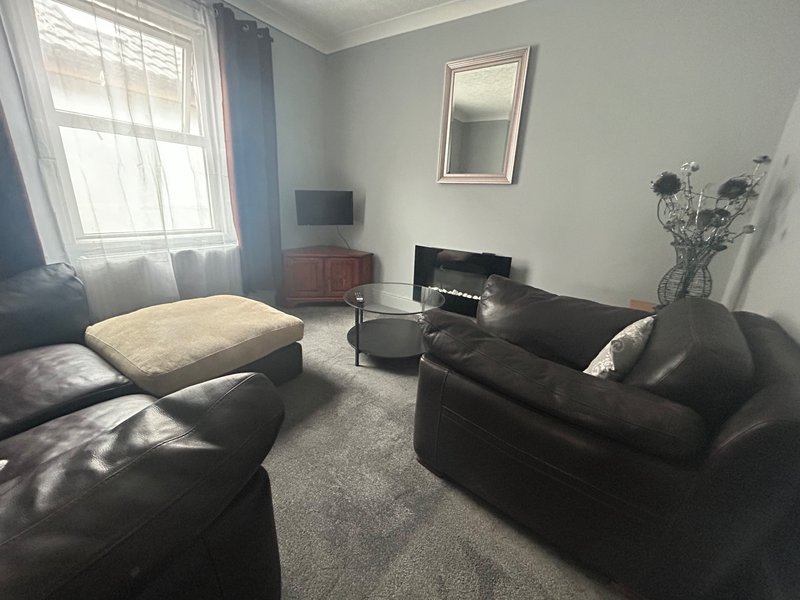 Comfortable living room with Smart TV, brown cosy leather sofas, fireplace, window with curtains