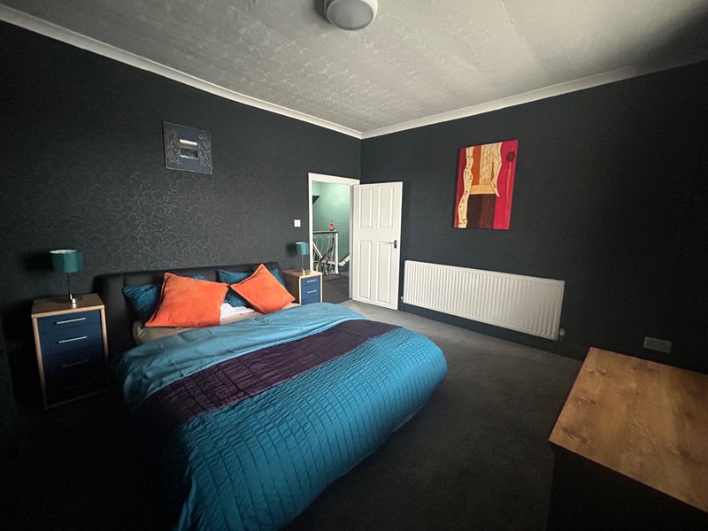 Modern bedroom with blue bedding, orange cushions, dark walls, storage cupboards and white radiator