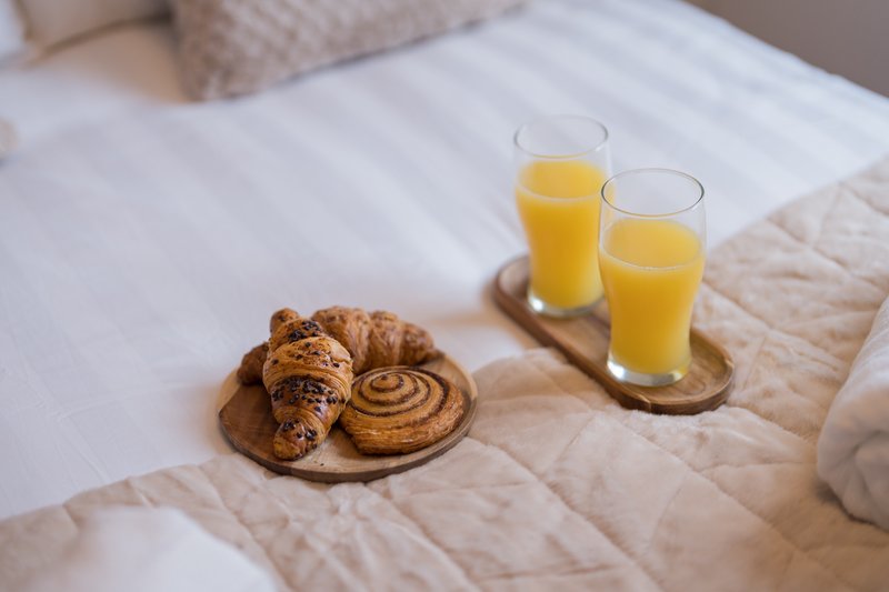 Breakfast tray on bed with croissant, pastry, and orange juice glasses