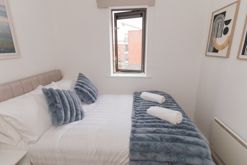 Bright bedroom with double bed, striped blue cushions and throw, window with city view
