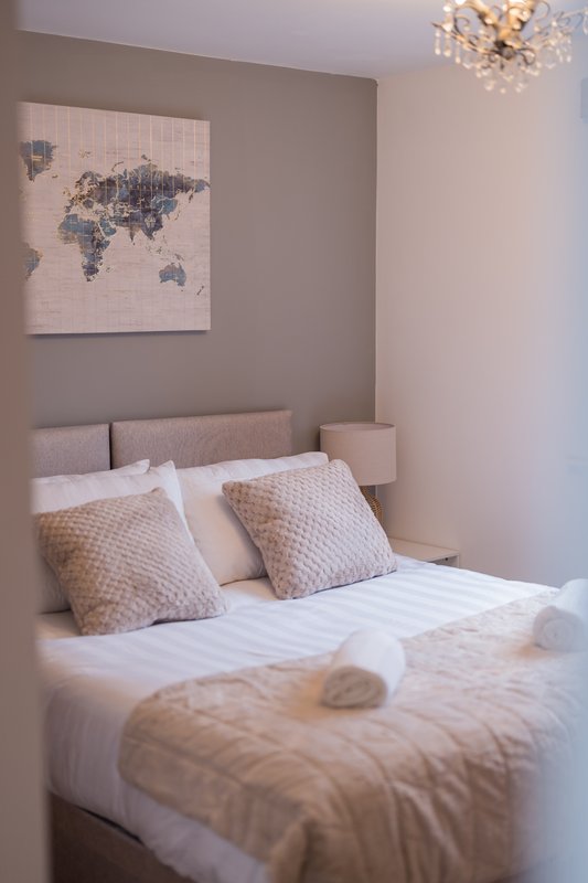 Neutral bedroom with double bed, decorative pillows, world map artwork and ceiling light