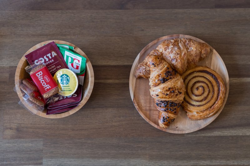 Wooden table with two bowls containing packaged snacks and fresh pastries