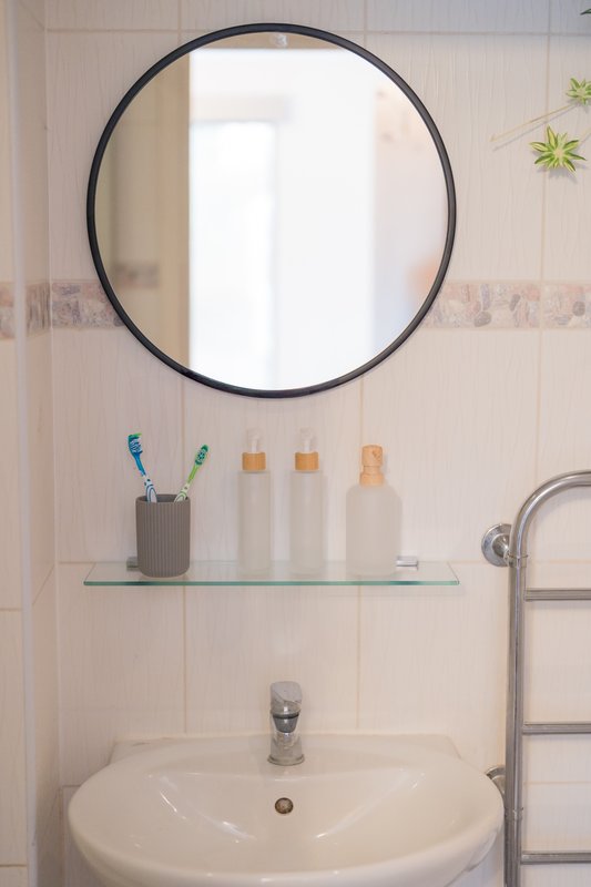 Bathroom with circular mirror, white sink, glass shelf with toiletries and toothbrushes
