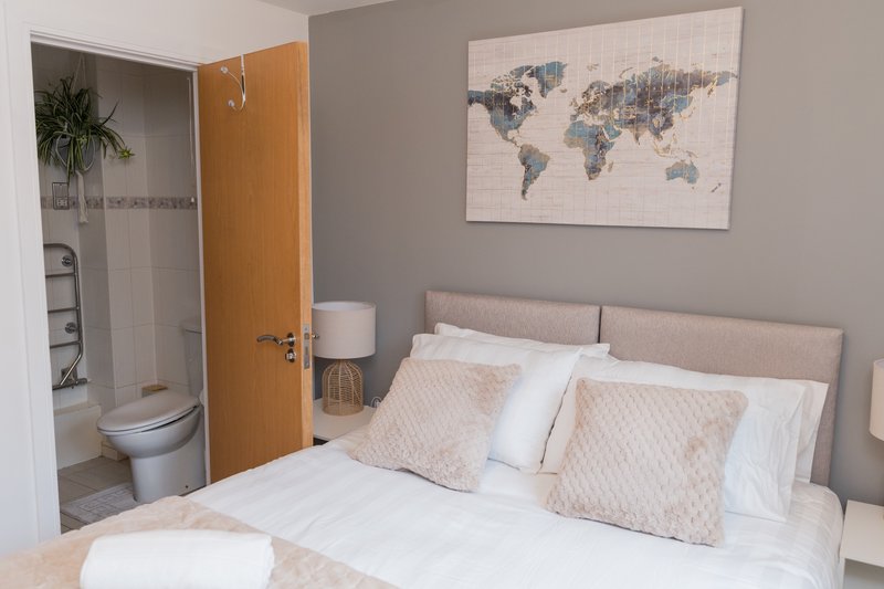 Bedroom with double bed, decorative pillows, world map artwork, and ensuite bathroom visible