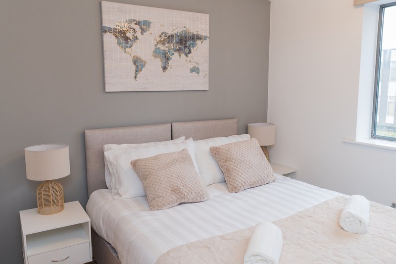 Modern bedroom with double bed, beige headboard, white bedding, decorative pillows and world map wall art