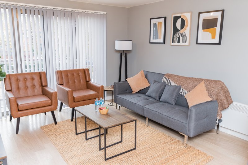 Modern living room with gray sofa, tan leather chairs, coffee table and wall art