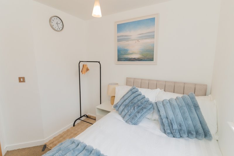 Bright bedroom with double bed, blue bedding, wall art, and wooden flooring