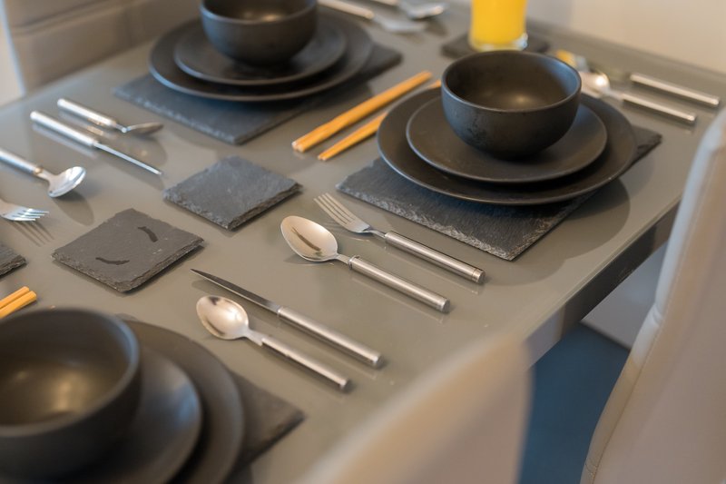 Dining table set with black plates, bowls, cutlery, and gold napkins