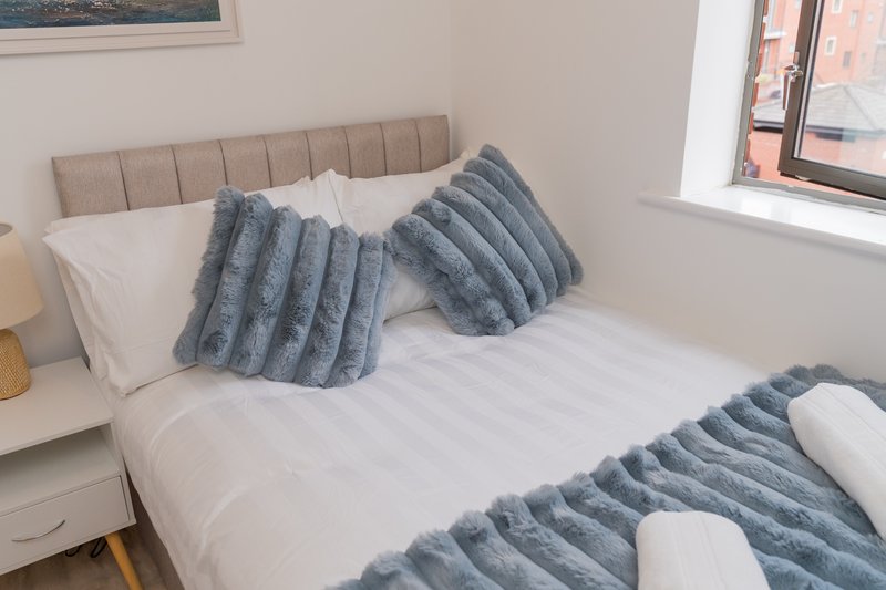 Modern bedroom with double bed, grey quilted headboard, white bedding and grey cushions