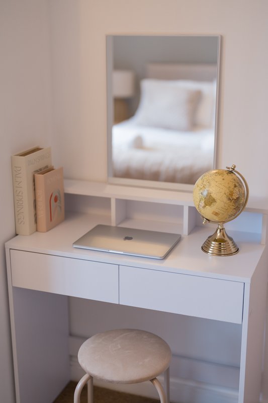 Minimalist bedroom desk with mirror, globe, laptop, books and stool