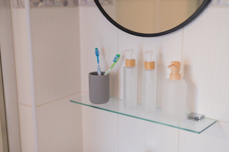 Bathroom shelf with toothbrushes, toiletries bottles, and circular mirror above