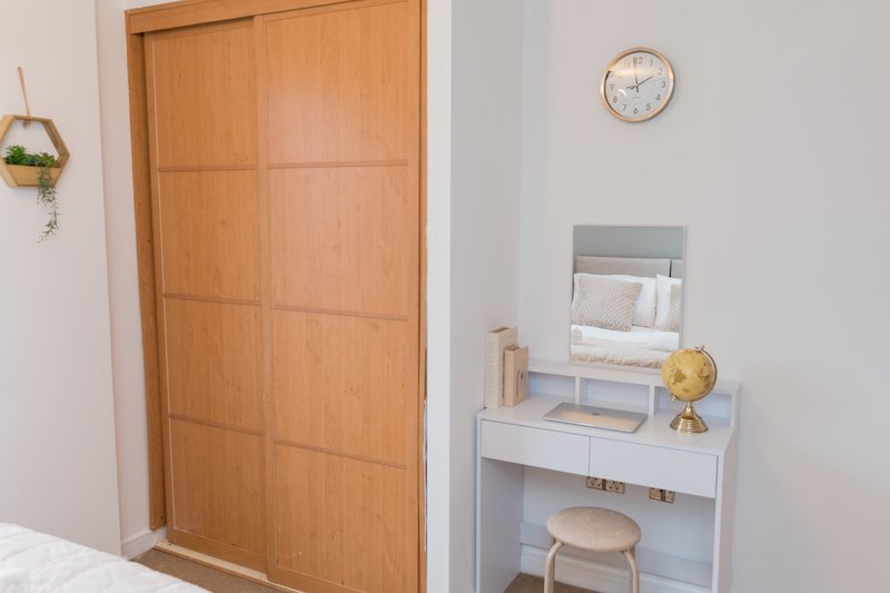 Bedroom with wooden wardrobe door, white desk, globe, and wall clock